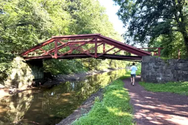 A red pedestrian bridge crossing a wooded stream in Lower Makefield Township.